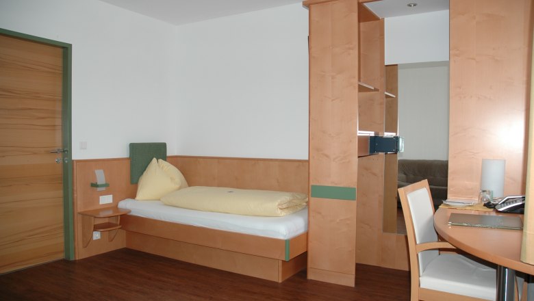 Hotel Zur Alten Schule, © Viregro Capital Gmbh A simply furnished hotel room with a single bed, desk and wooden paneling.