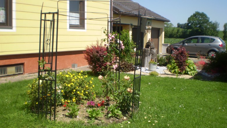 House Gerti, © Familie Hödelsberger A well-tended garden with a flower bed and trellis in front of a yellow house.