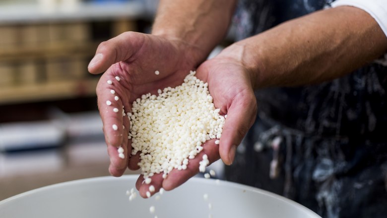 Candle manufactory, © Glaser Kerzen Close-up of hands holding white wax beads over a container.