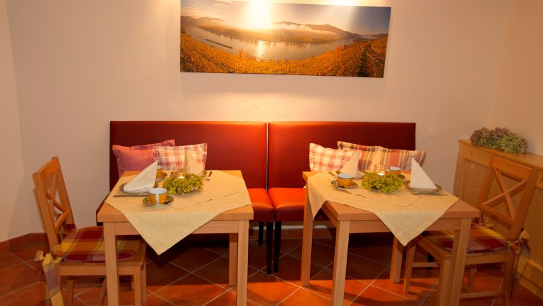 Breakfast room, © www.wachaufoto.at Cozy breakfast room with two set tables, red benches and a landscape painting on the wall.