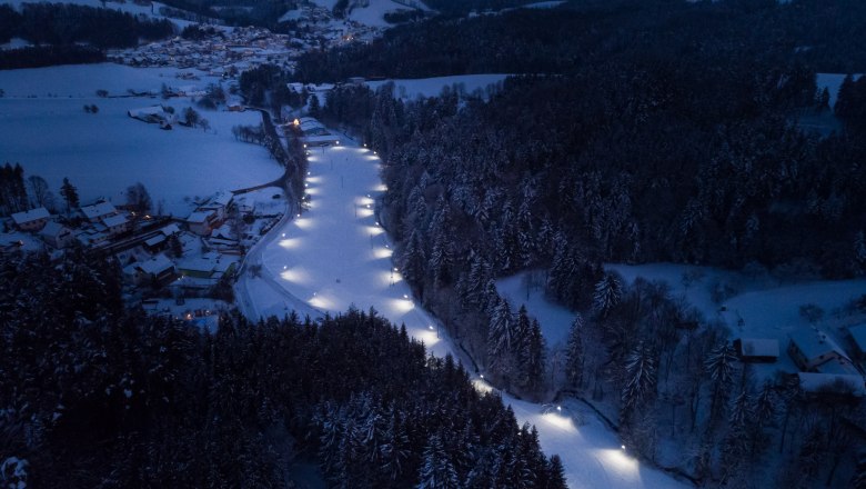 Floodlit trail in Zöbern, © Wiener Alpen, Martin Fülöp Aerial view of an illuminated cross-country ski trail in a snowy landscape at night.