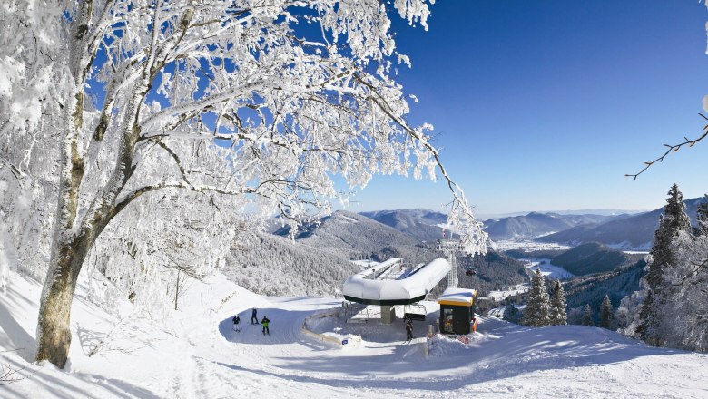 Summit station chair lift - © schneebergbahn.at, © schnneebergbahn.at Winter landscape with chairlift station, snow-covered trees and mountains in the background.