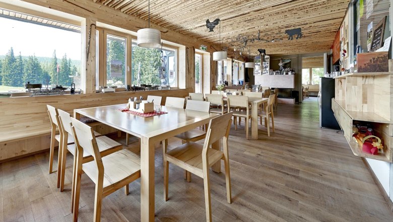 Interior view of the Knofeleben Naturefriends House, © Wiener Alpen / Bene Croy Interior of a Naturfreundehaus with wooden furniture and large windows overlooking the forest.