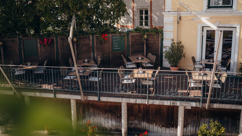 Bike-friendly inn on the Danube cycle path, © Niederösterreich Werbung/Daniela Führer Cozy terrace of a café with wooden tables and chairs, surrounded by plants.