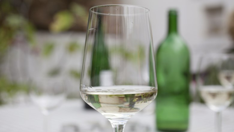 Wine glass, © Weinviertel Tourismus GmbH / Christine Wurnig A wine glass with white wine in the foreground, blurred green bottle in the background.