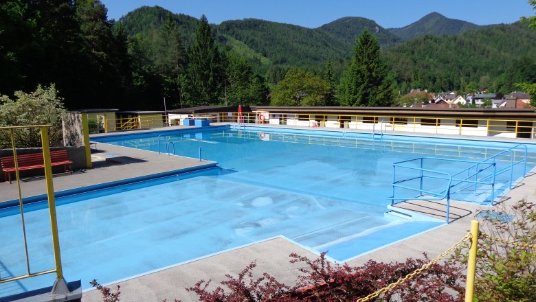 Hohenberg alpine spa, © Marktgemeinde Hohenberg An empty outdoor pool with blue water, surrounded by mountains and trees.
