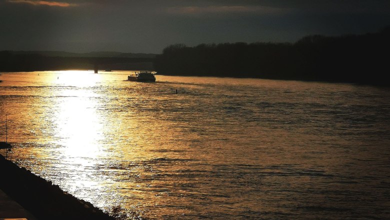 Sunset in front of the campsite, © Szilágyi Sunset over a river with a boat and dark clouds in the sky.