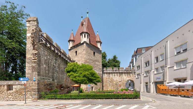 Stretching tower with private museum, © Wiener Alpen, Christoph Schubert Historic stretching tower with red roof and adjoining wall, surrounded by modern buildings and a road.