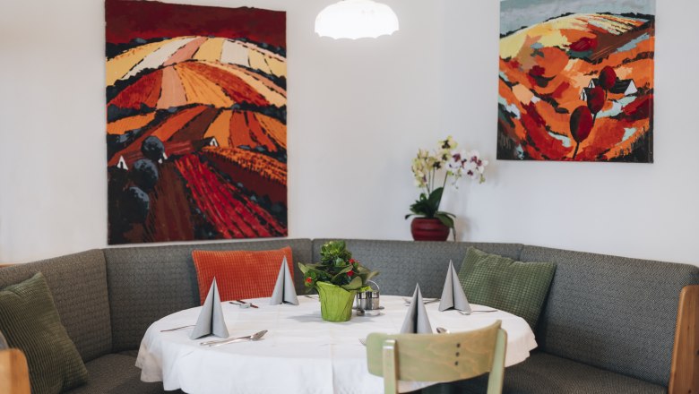 Inviting ambience to enjoy, © Niederösterreich Werbung/David Schreiber Cozy seating area with table, decorated with grey napkins and a plant, surrounded by colorful landscape paintings on the wall.