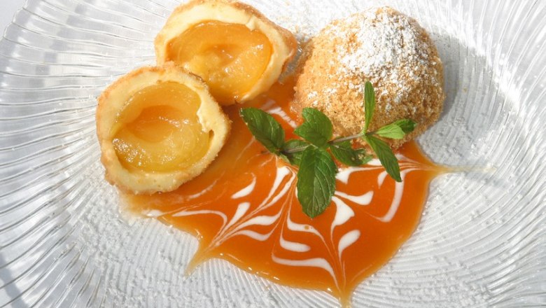Wachau apricot dumplings, © Hotel Richard Löwenherz Wachau apricot dumplings on a plate decorated with apricot sauce and mint leaves.