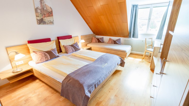 Guest room, © Annemarie Heller Cozy guest room with double bed, single bed, wood paneling and large window.