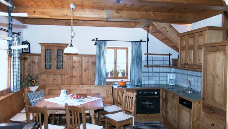 Kitchen, © Ferienhaus Hintereck Rustic kitchen with wooden furniture, dining table and chairs, stove, sink and window with checkered curtains.