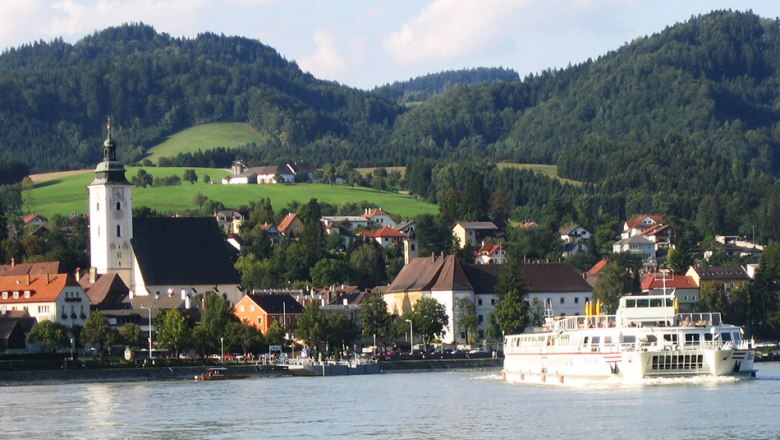 Grein 3 landing stage in Grein, © Donau Schiffsstationen GmbH Town of Grein with church and ship on the Danube, surrounded by hills.