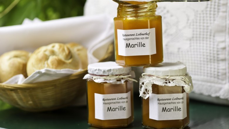 Products from Loibnerhof, © Rita Newman Three jars of apricot jam from the Loibnerhof restaurant next to a basket of bread rolls.