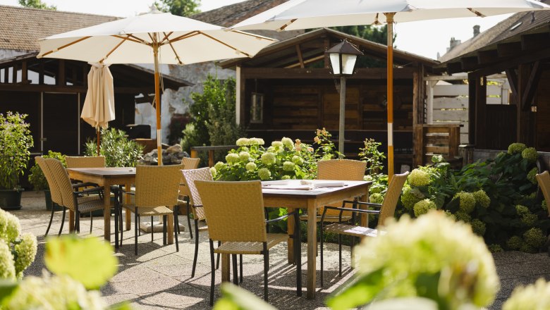 One of the most beautiful guest gardens in the Weinviertel, © Niederösterreich Werbung/Michael Reidinger An idyllic guest garden with wooden tables, chairs and parasols, surrounded by green plants and flowers.