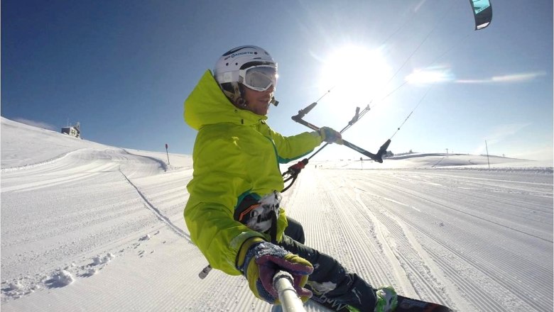 Snowkite courses, © Snowkitekurse.at Person snowkiting on a snowy slope with blue sky and sunshine.