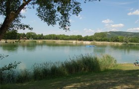 Bathing pond Seeschlacht, © Marktgemeinde Langenzersdorf A calm lake with reeds in the foreground and wooded hills in the background.