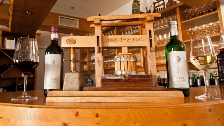 Tree press with wine bottle, © Vinterra Zöchling Wine bottles and glasses next to a small wooden press on a counter.