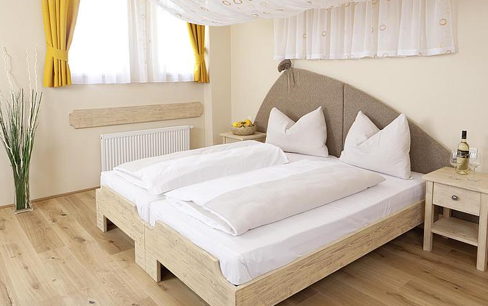 Guest room, © JUFA A cozy guest room with a double bed, yellow curtains and wooden furniture.