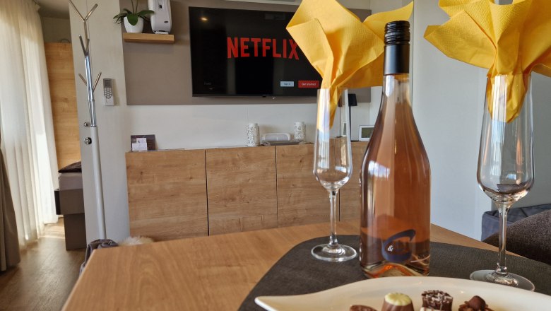 Kitchen table Johannesbachklamm Chalet, © Johannesbachklamm Chalet Interior view of a chalet with a bottle of wine, glasses and chocolates on a table, television in the background.
