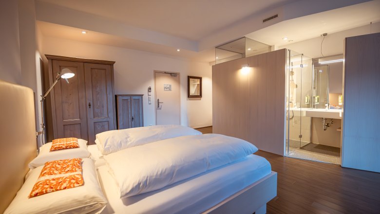 Refugium Hochstrass, © Niederösterreich Werbung / Maximilian Pawlikowsky Modern hotel room with double bed, wooden wardrobe and open bathroom.