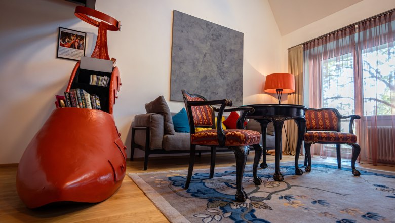 At the Park Hotel, © Niederösterreich Werbung / Maximilian Pawlikowsky A stylishly furnished hotel room with a large red shoe as a bookshelf, antique chairs, a table and a floor lamp.