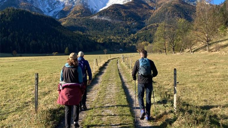 © Angelika Burger Four hikers on a dirt road with snow-covered mountains in the background.