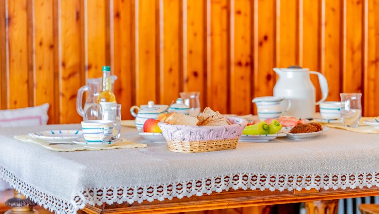 Woltron Manor, © Wiener Alpen / Christian Kremsl Breakfast table with crockery, bread, fruit and drinks in front of wood paneling.