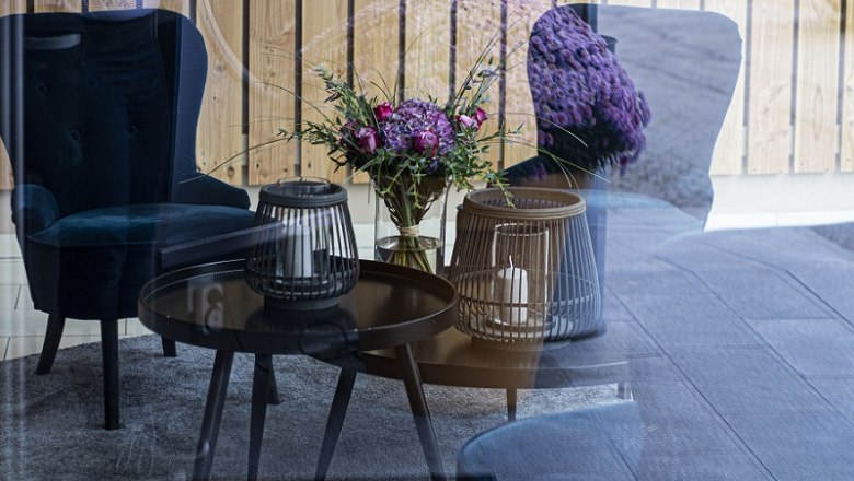 City Hotel Gürtler Lobby, © Doris Schwarz-König A cozy lounge area with blue armchairs, a table with candles and a bouquet of flowers, reflected in a glass wall.