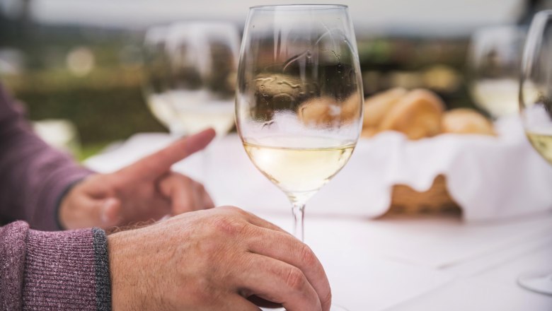 Wine enjoyment, © Donau NÖ/Daniela Matejschek Close-up of hands with wine glass on a laid table outdoors.