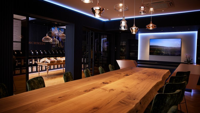 Wine lounge, © Ben Leitern Elegant room with a long wooden table, modern lamps and a screen on the wall.