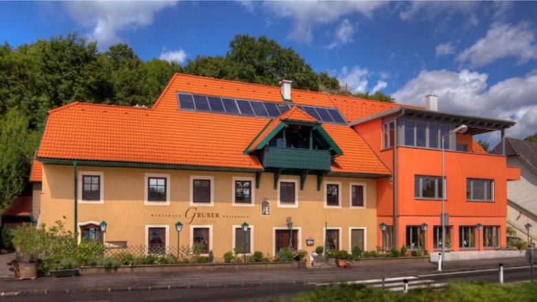 Tavern, © wirtshausgruber.at A traditional inn with an orange roof and solar panels, surrounded by green nature.