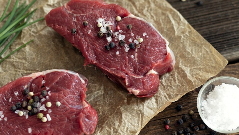Beef from Angus pasture cattle, © Fam. Luckerbauer Two pieces of raw beef sprinkled with salt and pepper on baking paper, next to chives, a bowl of salt and pepper.