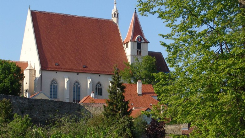 St. Stephen's parish church, © Stadt Eggenburg St. Stephen's parish church with red roof and tower, surrounded by trees and a stone wall.