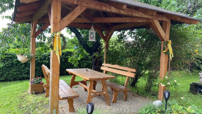 Arbor in the garden, © Wiener Alpen Wooden arbor in the garden with table and benches, surrounded by plants.