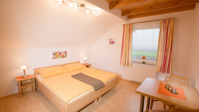 Vacation apartment Muck, © schwarz-könig.at Cozy bedroom with double bed, wooden beamed ceiling and table with chairs.