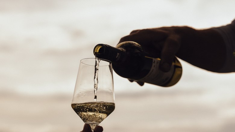 Pouring wine, © Weinviertel Tourismus / Sophie Menegaldo Wine is poured into a glass outdoors, with a landscape in the background.