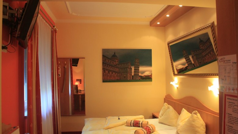 Double room, © Nimal Poudel Hotel room with a double bed, pictures of the Leaning Tower of Pisa and a TV on the wall.