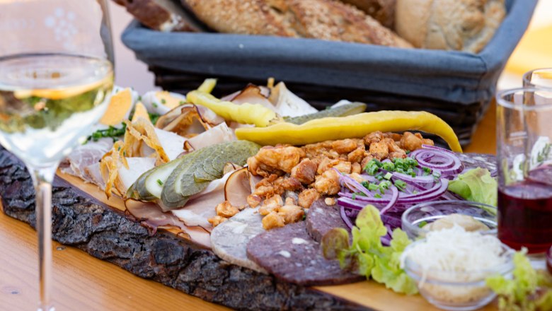 Heurigen platter, © Weinviertel Tourismus GmbH / Schwarz-König Heurigen platter with sausage, cheese, onions and bread on a wooden table.