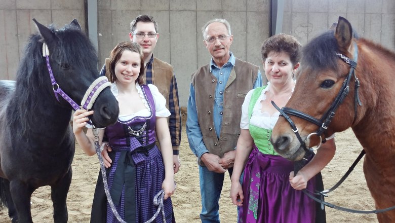 Family photo riding experience, © RMH A family in traditional dress stands with two horses in an indoor riding arena.