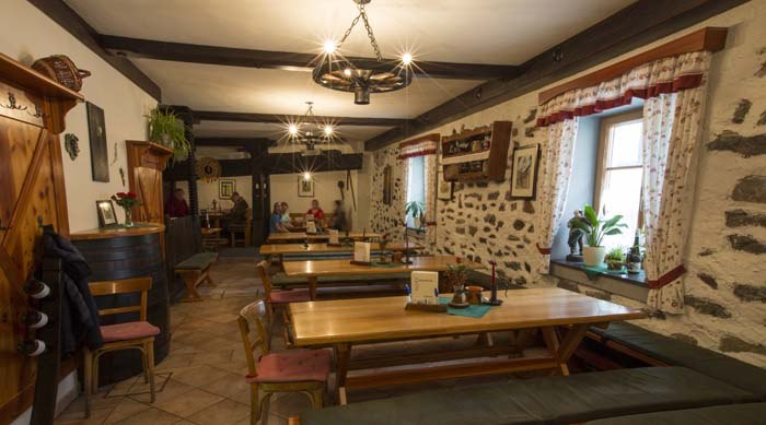 12b4566, © Josef Salomon Cozy dining room with wooden tables and stone walls.