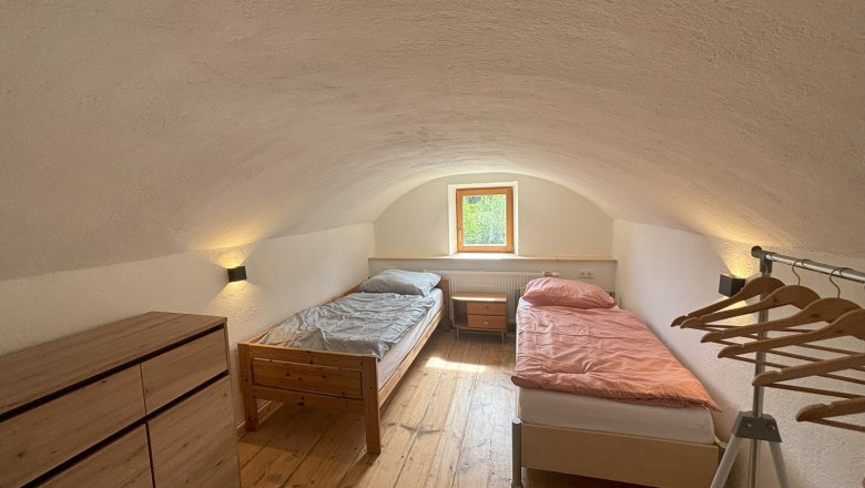 Double room, © Michael Hofer A simple double room with two single beds, a chest of drawers and a clothes rack. A small window lets in natural light.