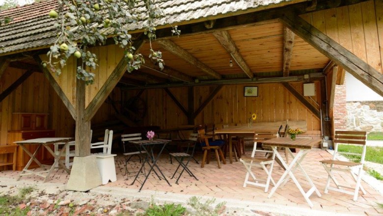 Pergola, © Martina Heilingsetzer Covered terrace with wooden tables and chairs, surrounded by wooden walls and an apple tree in the foreground.