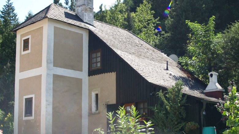 avaturm, © Gemeinde Furth An old house with a small tower and chimney, surrounded by trees and plants.