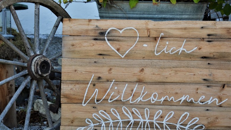 Welcome to the Höblinghof, © Gluschitz-Goebel Wooden sign with the inscription 'Welcome' and a heart symbol, next to it an old wagon wheel.