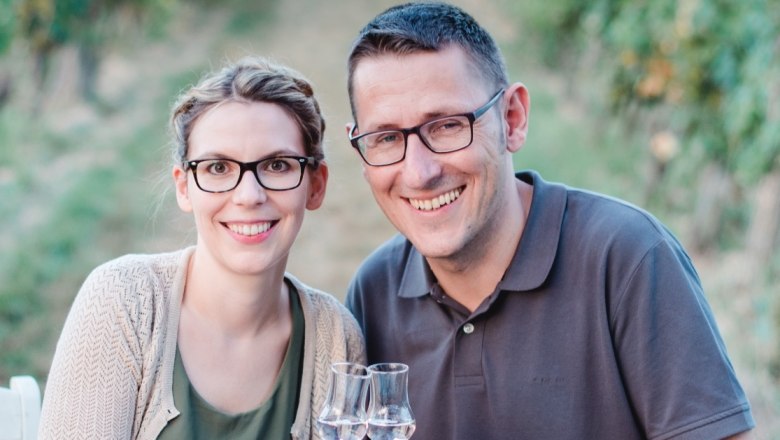 Kraus distillery, © Conny Beisteiner A smiling couple with glasses toast with shot glasses, blurred nature in the background.