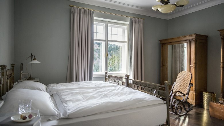 Villa Antoinette, © Matthias Kronfuss Elegant bedroom with antique bed, rocking chair and large window with curtains.
