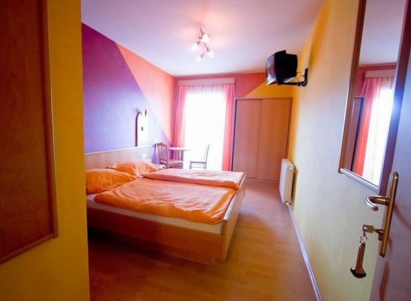 Pension Koderholt, © Koderholt A cozy guest room with a double bed, colorful walls and a small TV on the wall.