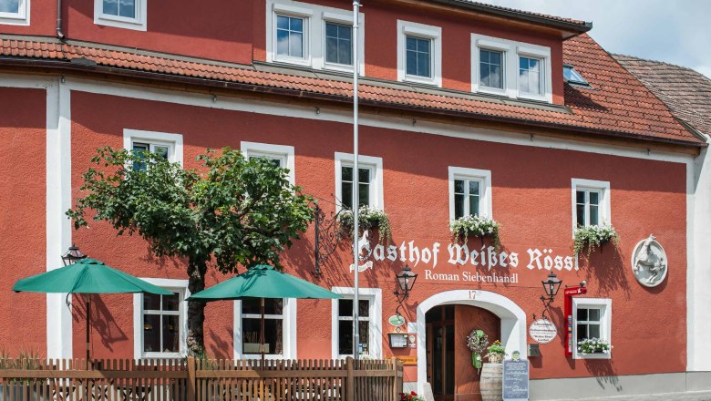 House view, © Martina Siebenhandl Red building with white window frames and green parasols in front of the entrance.