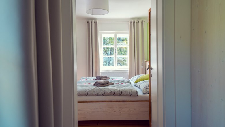 Guest rooms that invite you to stay longer, © Schlosstaverne Lunz/Martin Stellnberger A cozy guest room with a double bed, bed linen with deer motifs and folded towels on the bed, seen through an open door.